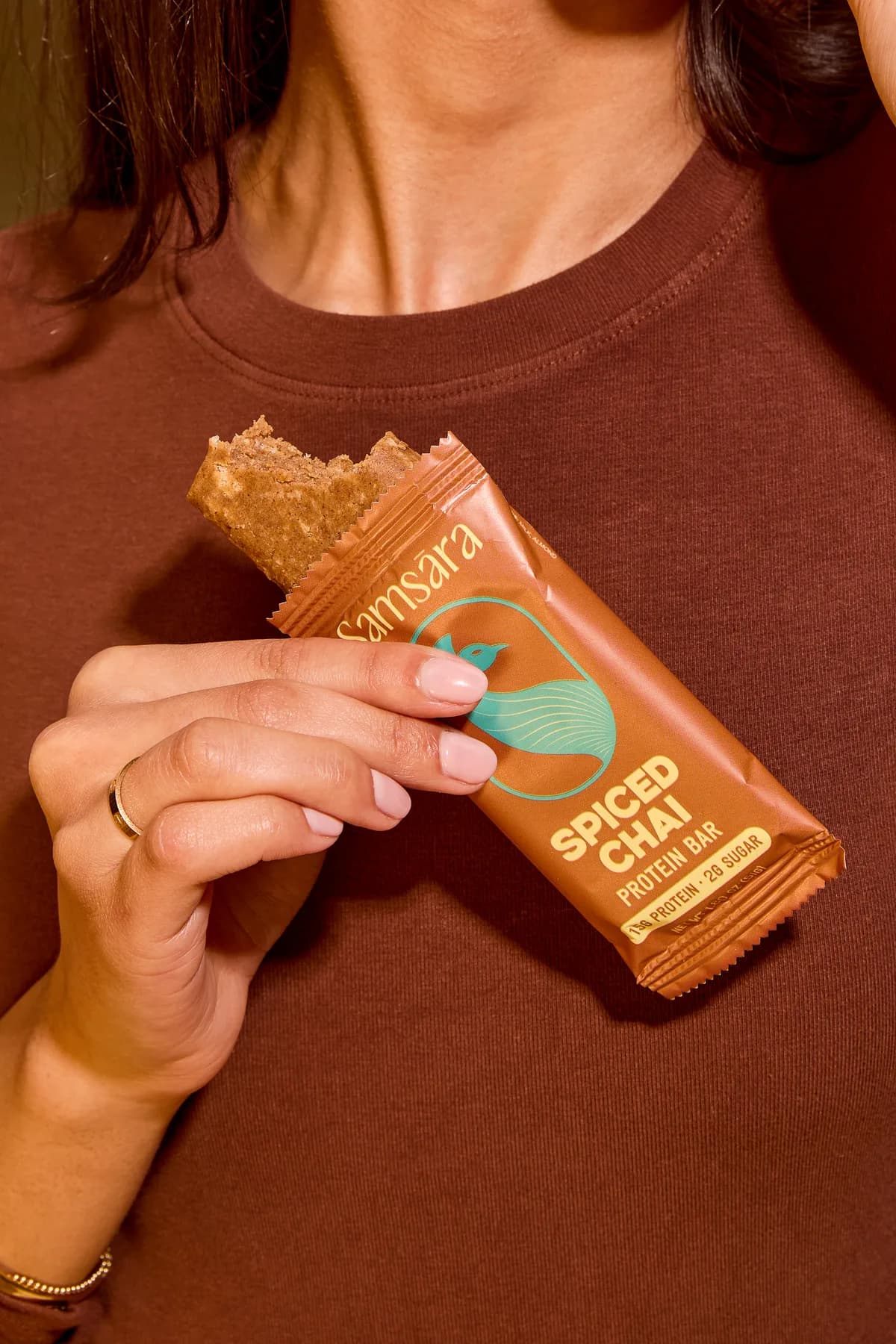 Hand holding a Spiced Chai protein bar with a bite taken